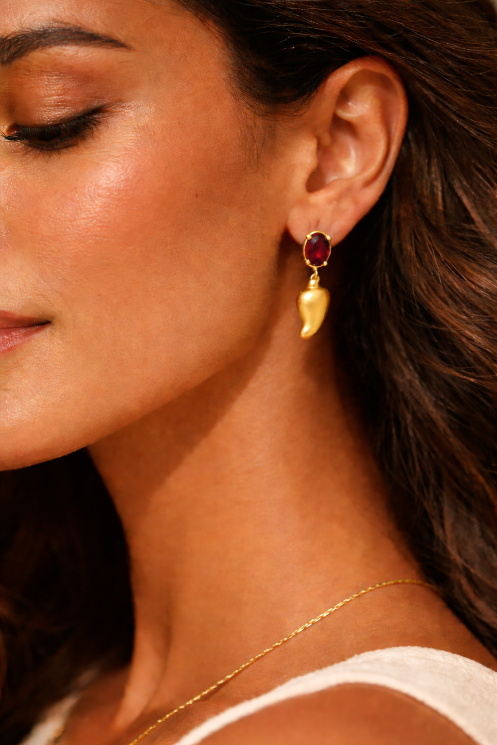 Close-up of a woman wearing gold earrings with a red gemstone.