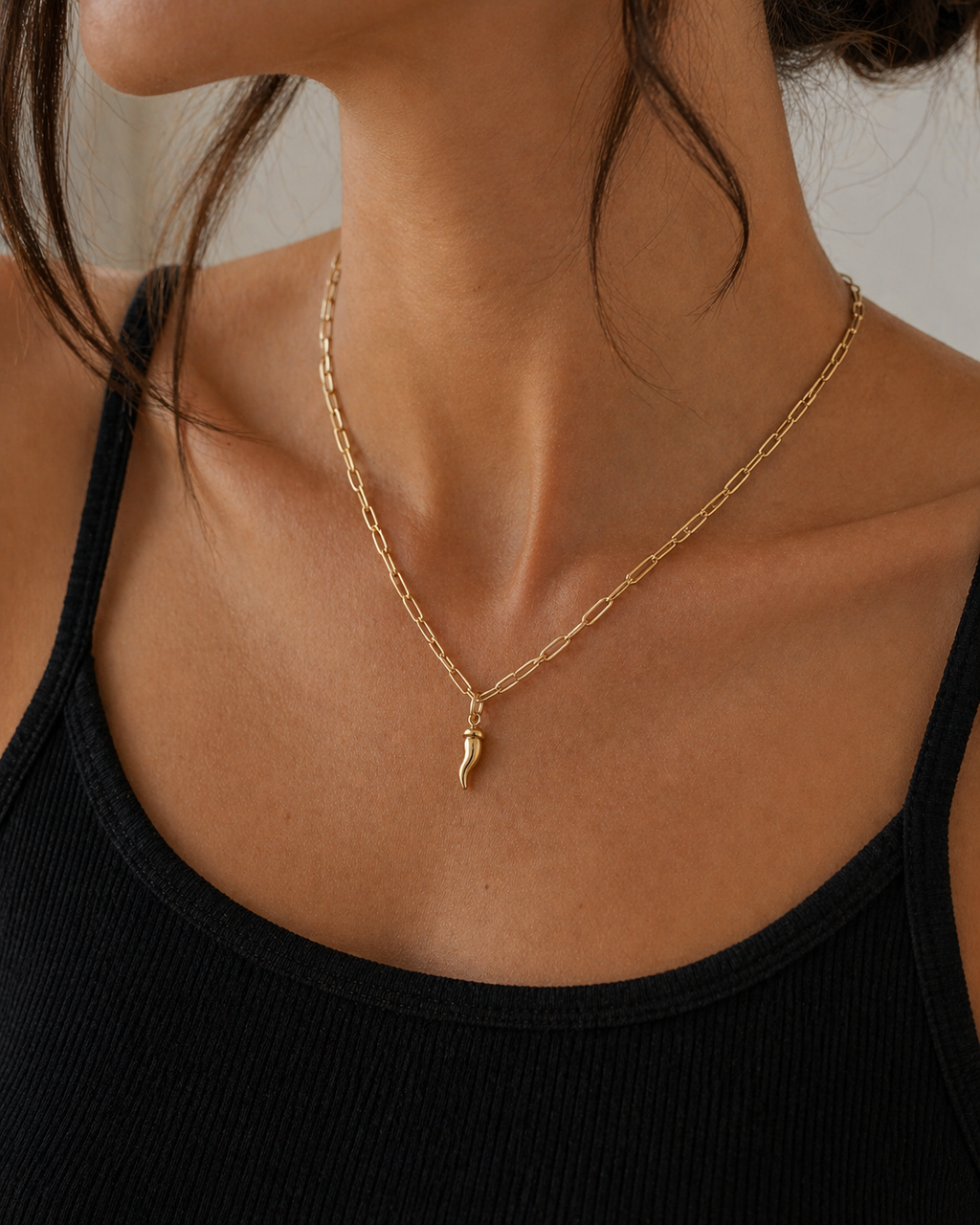Gold necklace with a pendant worn by a person in a black top against a neutral background